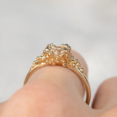 Side view of a gold ring featuring a central sparkling round old European cut diamond, surrounded by gold granules worn on a finger.