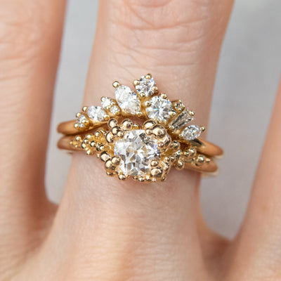 A gold ring featuring a central sparkling round old European cut diamond, surrounded by gold granules, stacked with a contoured diamond wedding band.