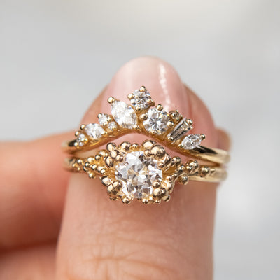 A gold ring featuring a central sparkling round old European cut diamond, surrounded by gold granules, stacked with a contoured diamond wedding band.