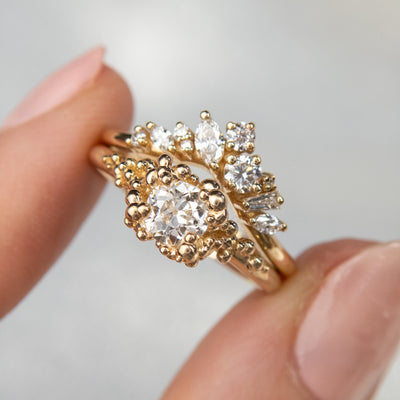 A gold ring featuring a central sparkling round old European cut diamond, surrounded by gold granules, stacked with a contoured diamond wedding band.