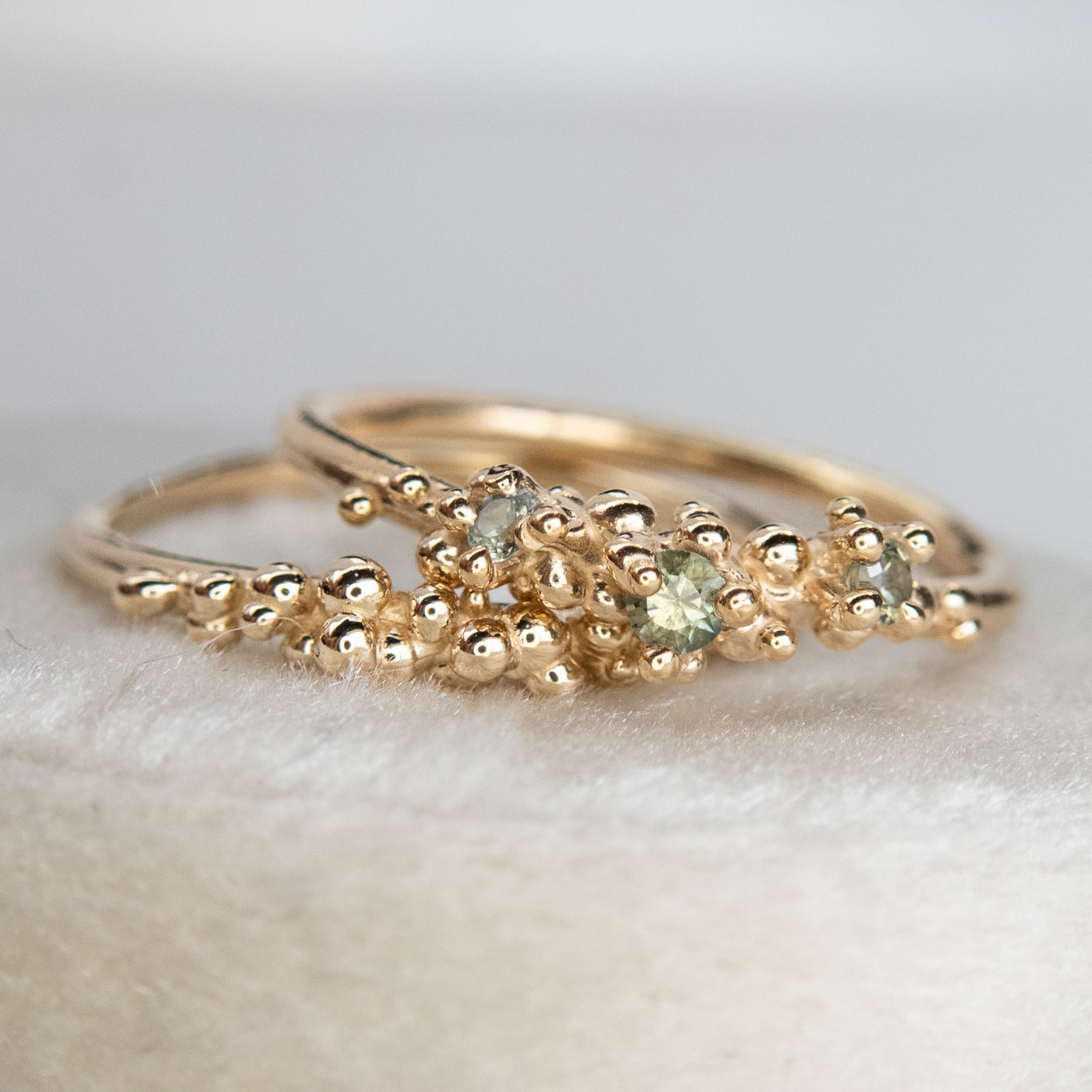 Stack of gold rings with organic detailing and gold bubbles, resting on a white velvet surface.