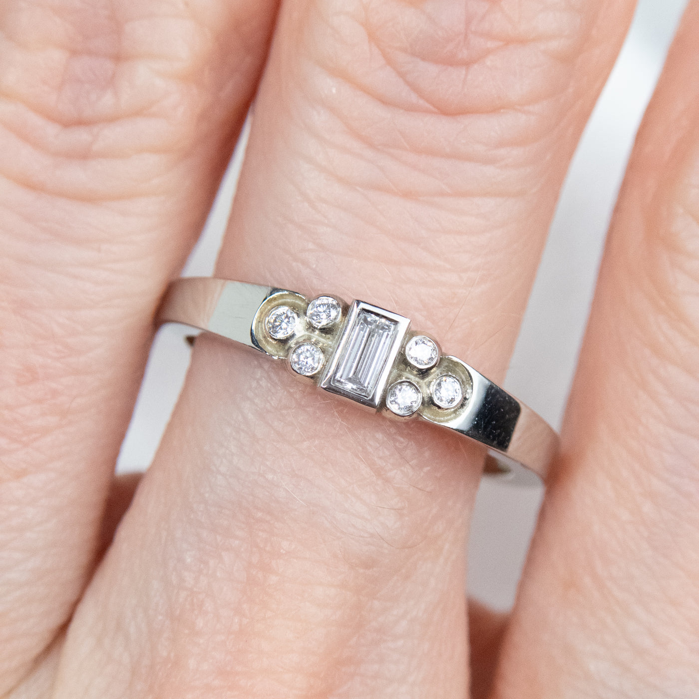 Elegant white gold ring with a central rectangular-cut diamond flanked by six small round diamonds, worn on a finger. 