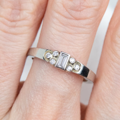 Elegant white gold ring with a central rectangular-cut diamond flanked by six small round diamonds, worn on a finger. 
