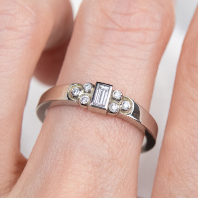 Elegant white gold ring with a central rectangular-cut diamond flanked by six small round diamonds, worn on a finger. 