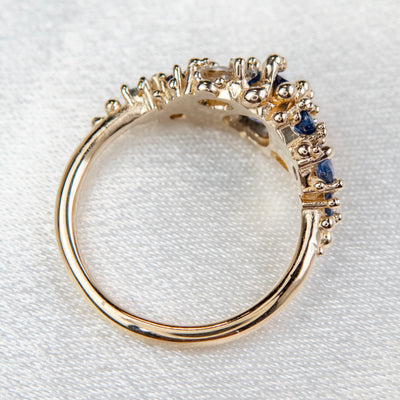 Intricately designed gold cluster ring featuring blue and colourless sapphires, set atop a soft fabric backdrop.