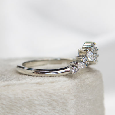 A delicate white gold ring featuring a cluster of sparkling diamonds in various shapes, elegantly set on a soft, light-colored surface shown from the side.
