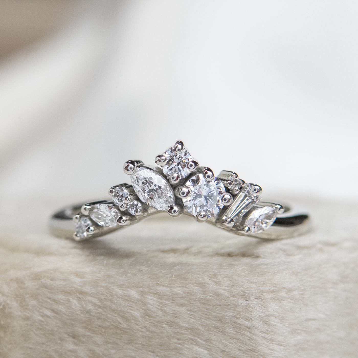 A delicate white gold ring featuring a cluster of sparkling diamonds in various shapes, elegantly set on a soft, light-colored surface.