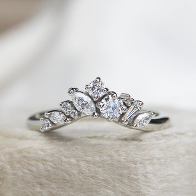 A delicate white gold ring featuring a cluster of sparkling diamonds in various shapes, elegantly set on a soft, light-colored surface.