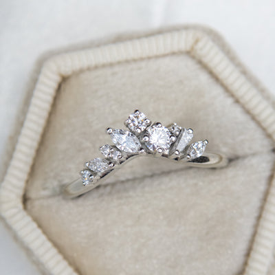A delicate white gold ring featuring a cluster of sparkling diamonds in various shapes, elegantly set in a white velvet ring box shown from above.