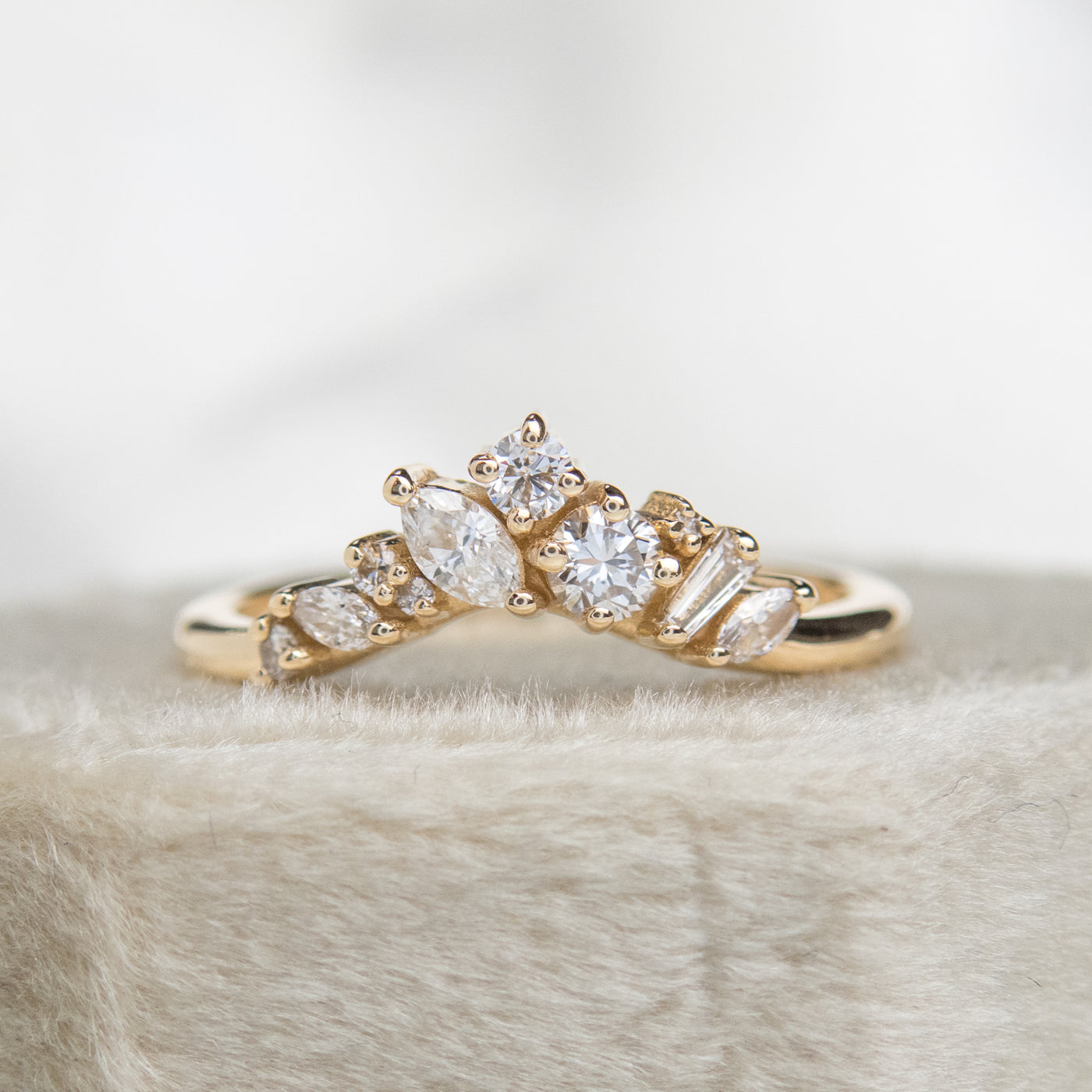 A delicate 14kt gold ring featuring a cluster of sparkling diamonds in various shapes, elegantly resting on a white velvet ring box.