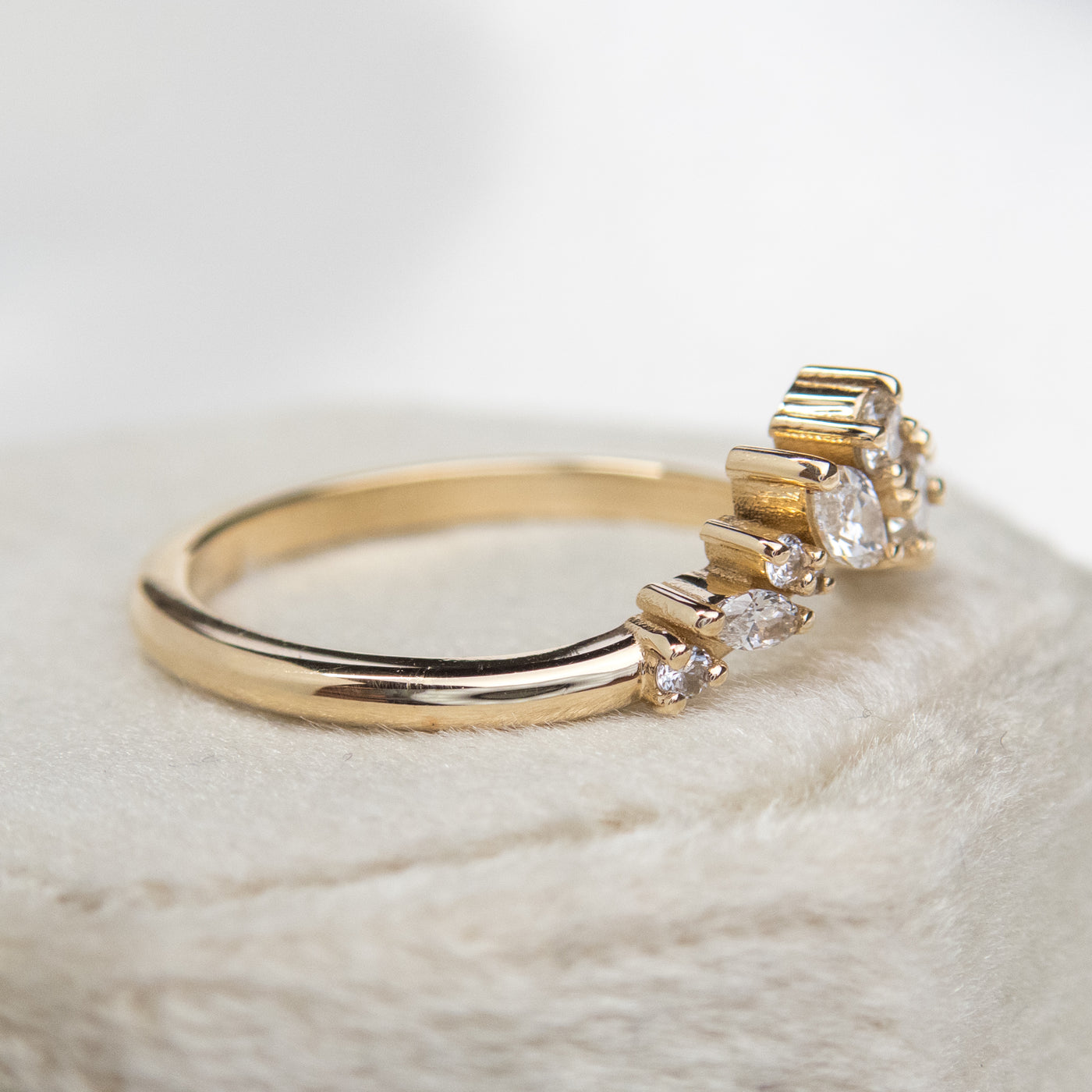 A delicate 14kt gold ring featuring a cluster of sparkling diamonds in various shapes, elegantly resting on a white velvet ring box shown from the side.