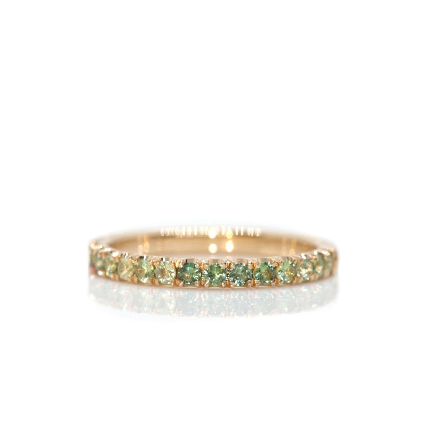 A delicate 14kt gold ring adorned with  brilliant cut parti-green sapphires in a variety of tones, reflecting beautifully against a white background.