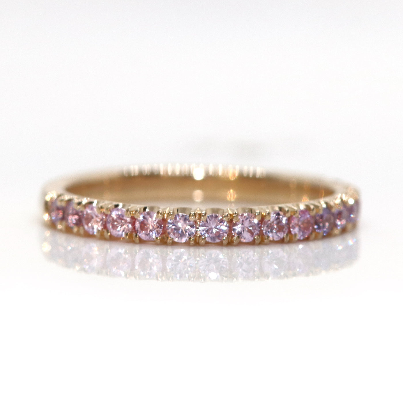 A delicate 14kt gold ring adorned with  brilliant cut pink sapphires in a variety of tones, reflecting beautifully against a white background.