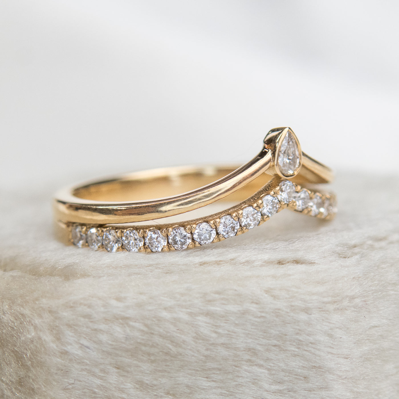 A delicate 14kt gold ring featuring a double peak design, adorned with sparkling pave diamonds and a pear diamond centerpiece, shown from the side lying on a velvet ring box.