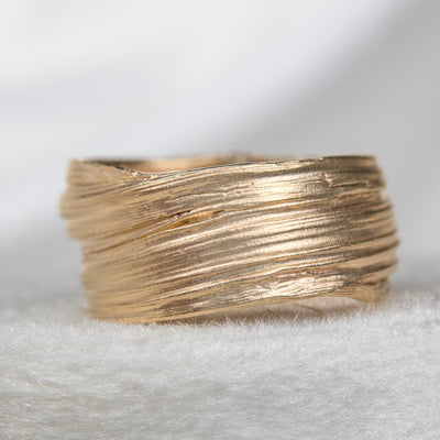 Gold textured ring with layered design, resting on a white velvet ring box, showcasing a modern and elegant aesthetic.