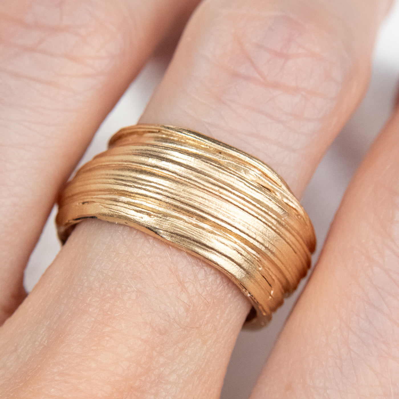 Gold textured ring with layered and organic design, shown on a finger, showcasing a modern and elegant aesthetic.