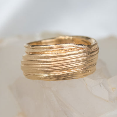 Gold textured ring with layered design, resting on a translucent crystal surface, showcasing a modern and elegant aesthetic.