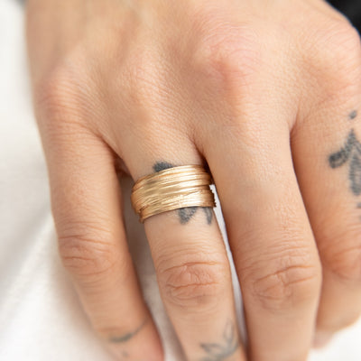 Gold textured ring with layered and organic design, shown on a finger with hand tattoos , showcasing a modern and elegant aesthetic.