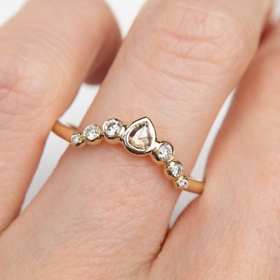 A delicate gold ring with a central pear-shaped diamond, flanked by smaller round diamonds worn on a finger.