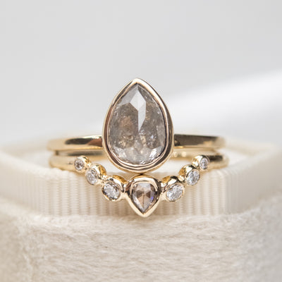 A stunning set of gold rings featuring a large pear-shaped salt & pepper diamond and delicate, smaller diamonds arranged elegantly.