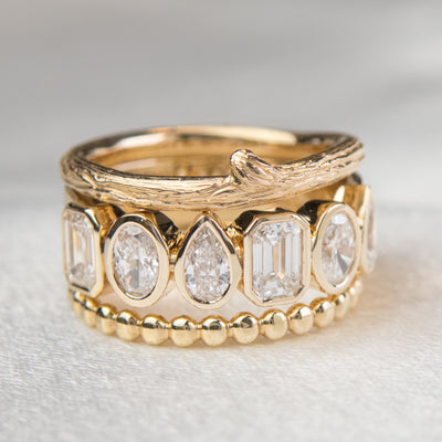 A stylish gold bezel ring adorned with various  lab diamond, including pear and emerald cuts, stacked with a gold beaded band and textured twiggy band.