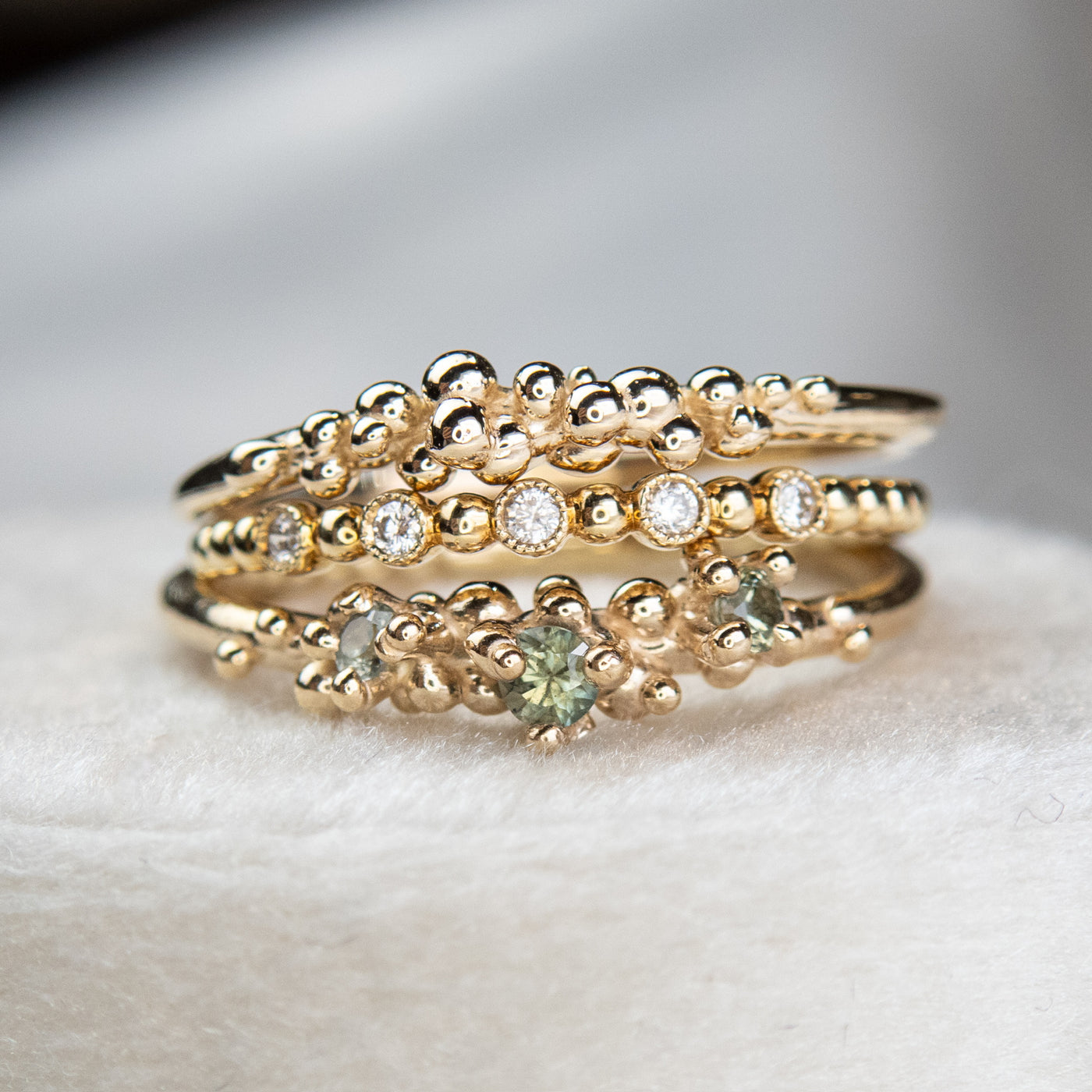 Stack of various gold rings, some with green sapphires and others with diamond details.
