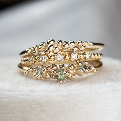 Stack of various gold rings, some with green sapphires and others with diamond details.