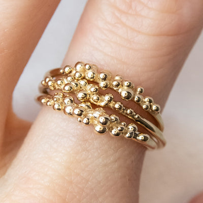 Three yellow gold stacking rings shown together on a finger, each with organically placed gold bubbles.