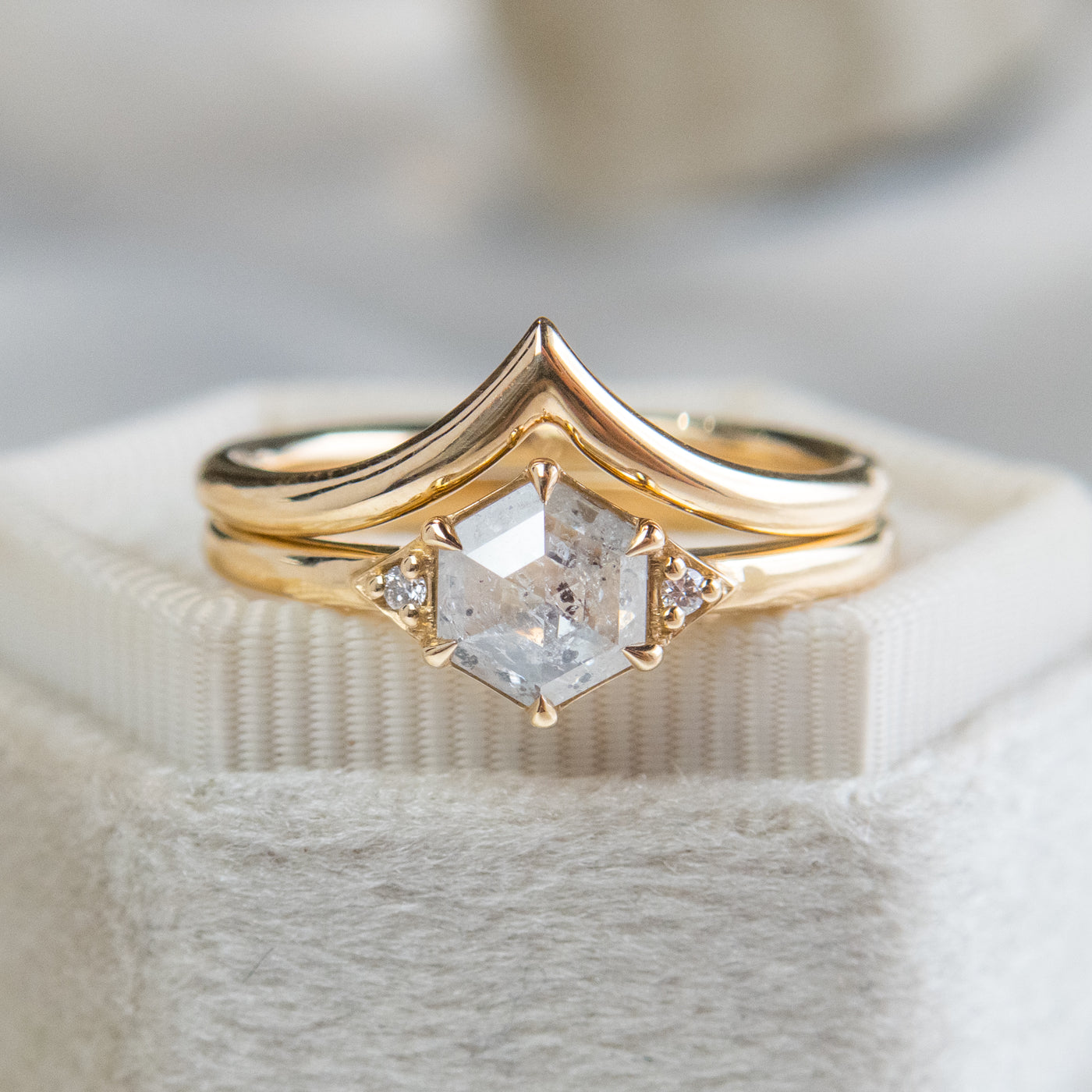 A gold ring with a hexagonal salt and pepper diamond, flanked by small round diamonds on either side, paired with a 'V' shaped gold band. 