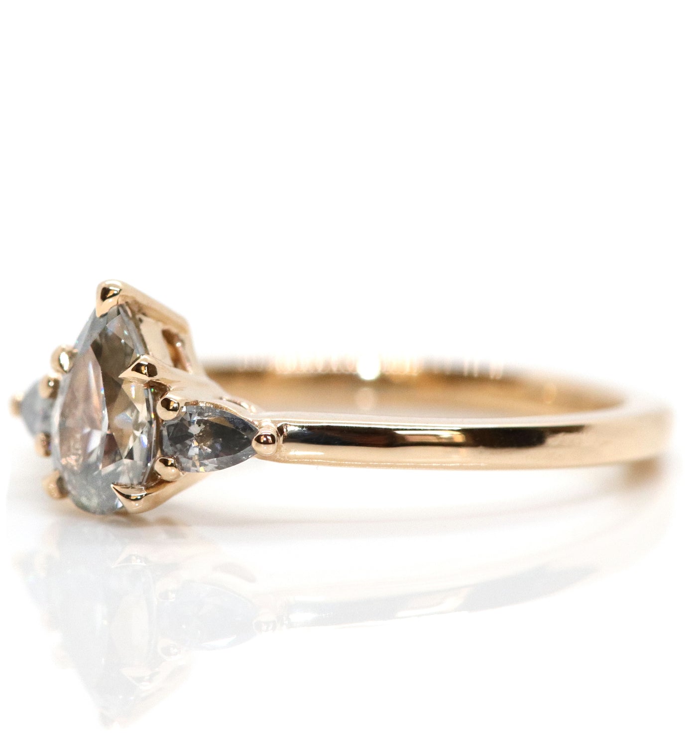 A gold three-stone ring with a fancy grey pear-shaped diamond center and two smaller grey pear-shaped side diamonds, on a white background. . 