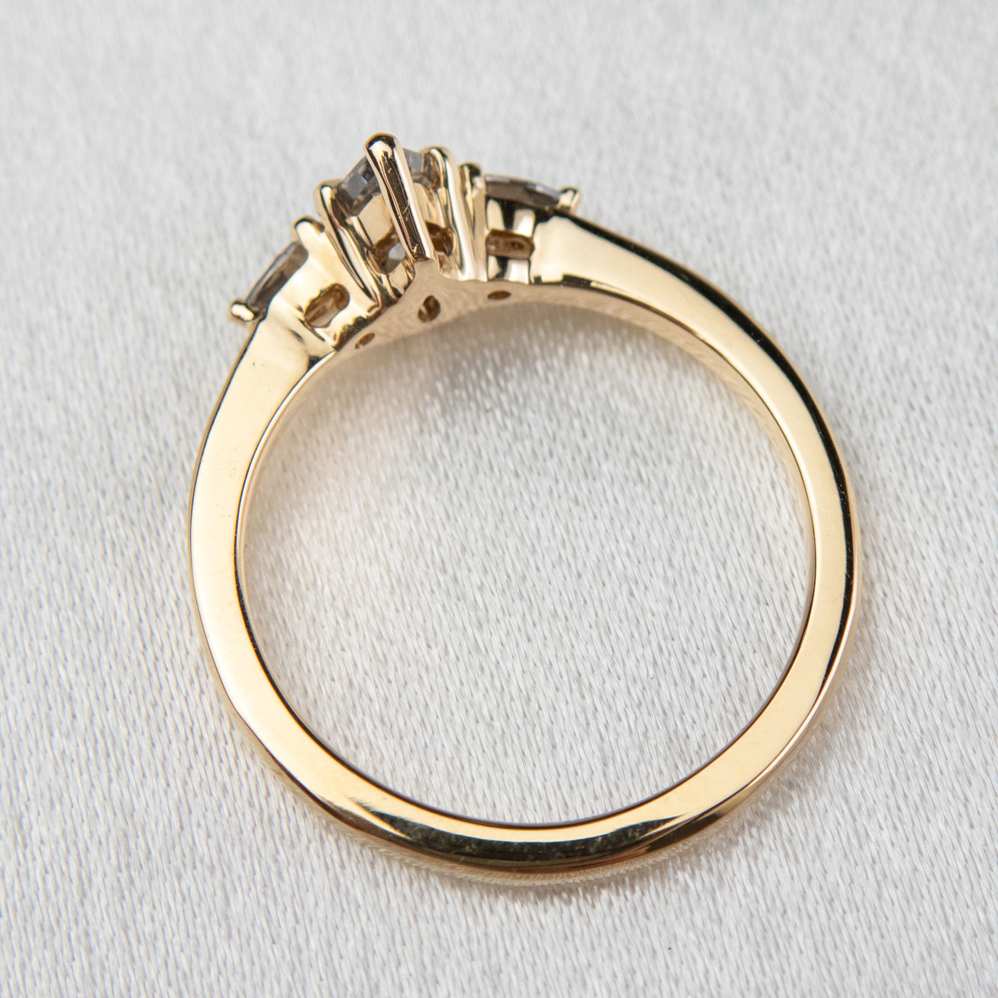 A side profile view of a gold three-stone ring with a fancy grey pear-shaped diamond center and two smaller grey pear-shaped side diamonds on a soft, textured surface.