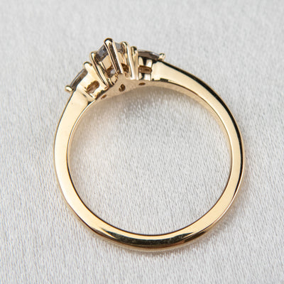 A side profile view of a gold three-stone ring with a fancy grey pear-shaped diamond center and two smaller grey pear-shaped side diamonds on a soft, textured surface.