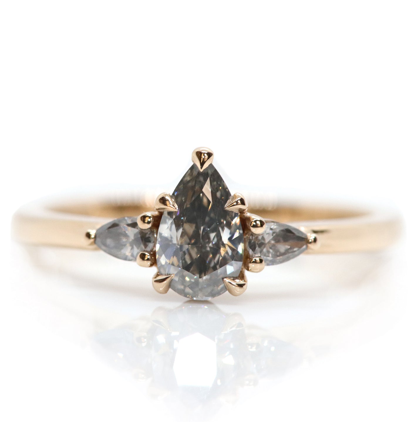 A gold three-stone ring with a fancy grey pear-shaped diamond center and two smaller grey pear-shaped side diamonds, on a white background. . 