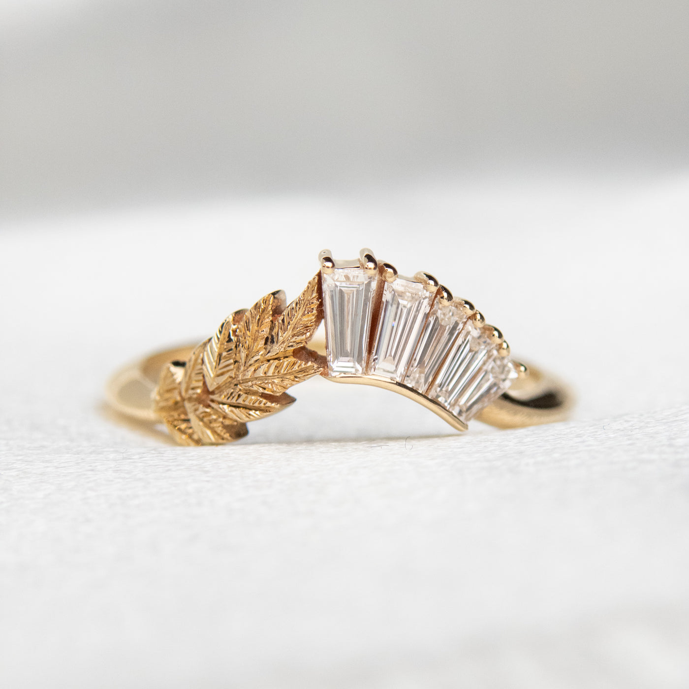 A curved gold ring featuring a hand engraved leaf design and a row of sparkling, baguette cut lab grown diamonds - it can be worn as an wedding band or stacked with other rings.