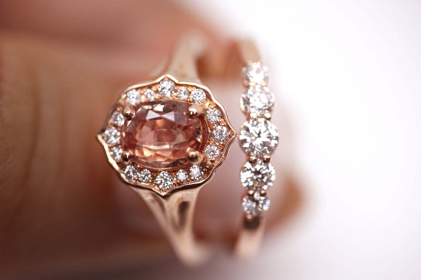 Elegant ring with an oval brilliant cut pink sapphire surrounded by a halo of small diamonds set in rose gold, against a white background. 