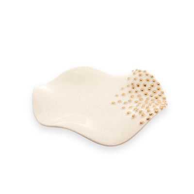 A smooth, white, dish-shaped jewelry tray adorned with small golden beads.