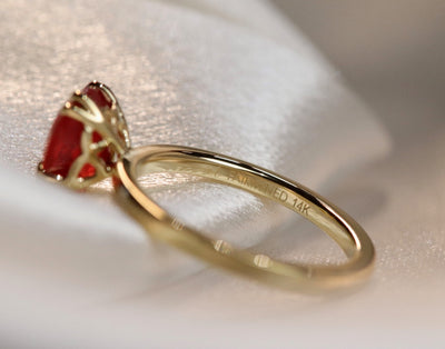 A close-up side view of a gold ring featuring an oval-cut red sapphire, elegantly set in delicate double claw prongs. 