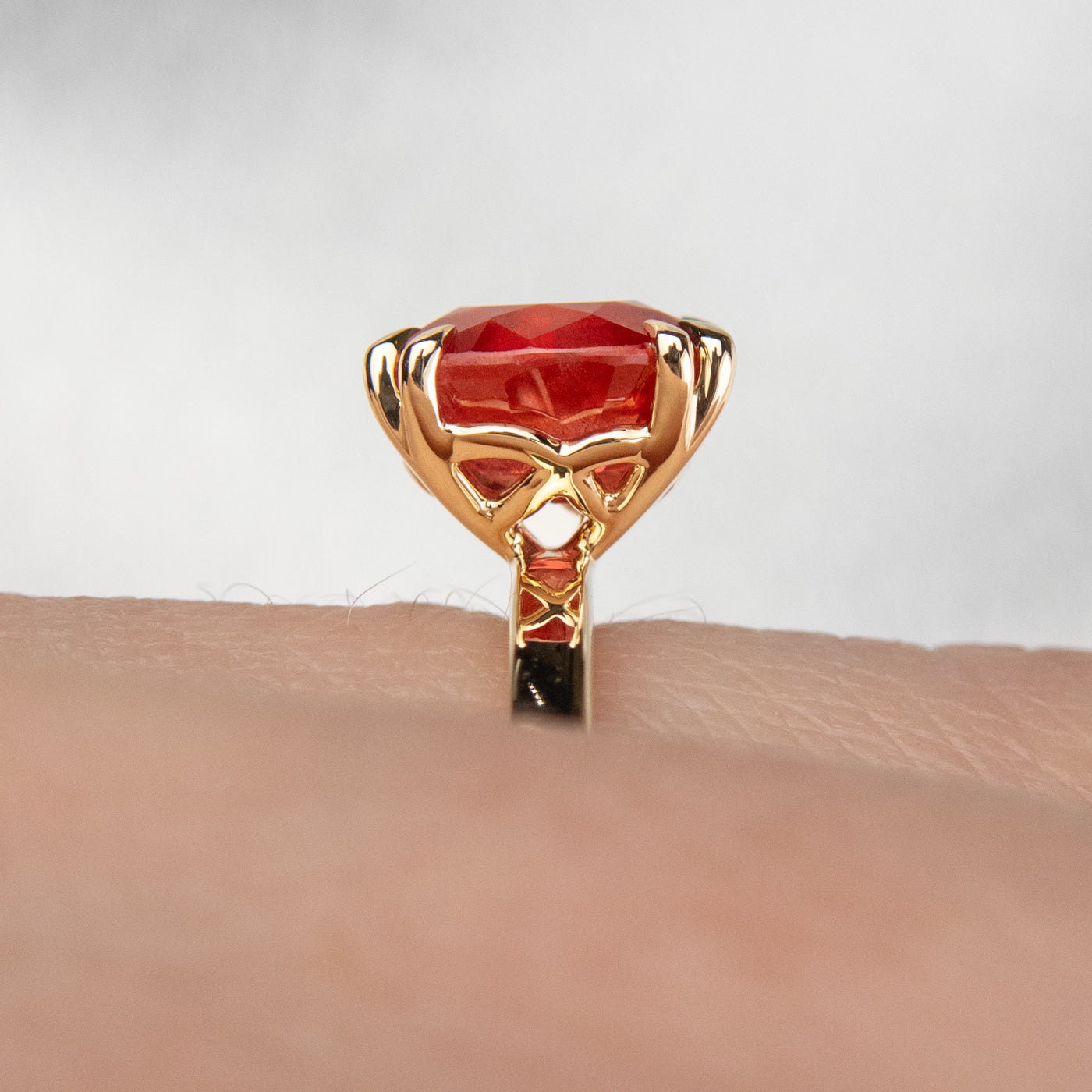 A close-up side view of a gold ring featuring an oval-cut red sapphire, elegantly set in delicate double claw prongs. Worn on a finger. 