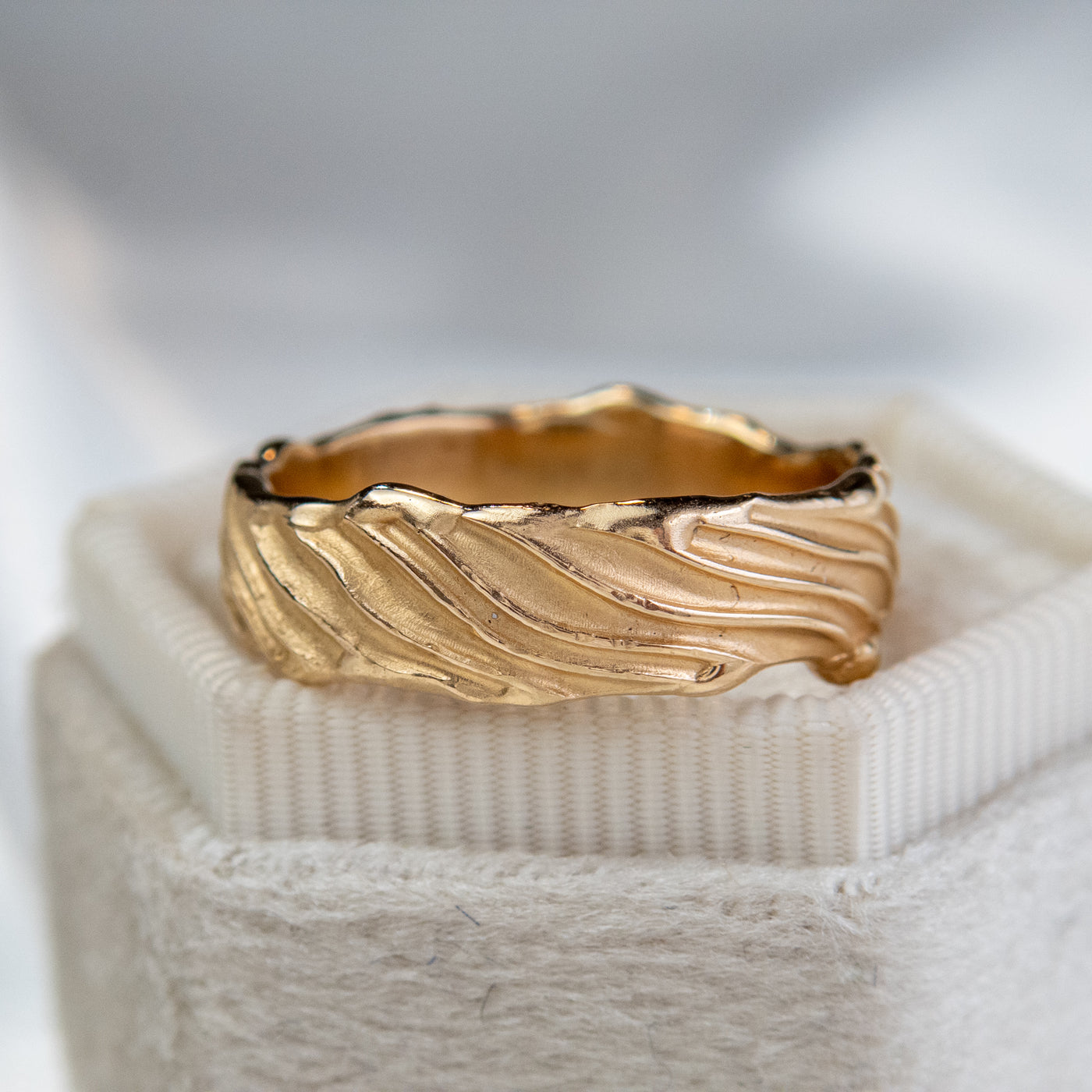 A 14kt gold wedding ring with intricate wave-like engravings, resting elegantly on velvet ring box.