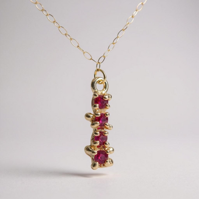 Gold necklace with a pendant featuring four round rubies encrusted in gold, on a light gray background.