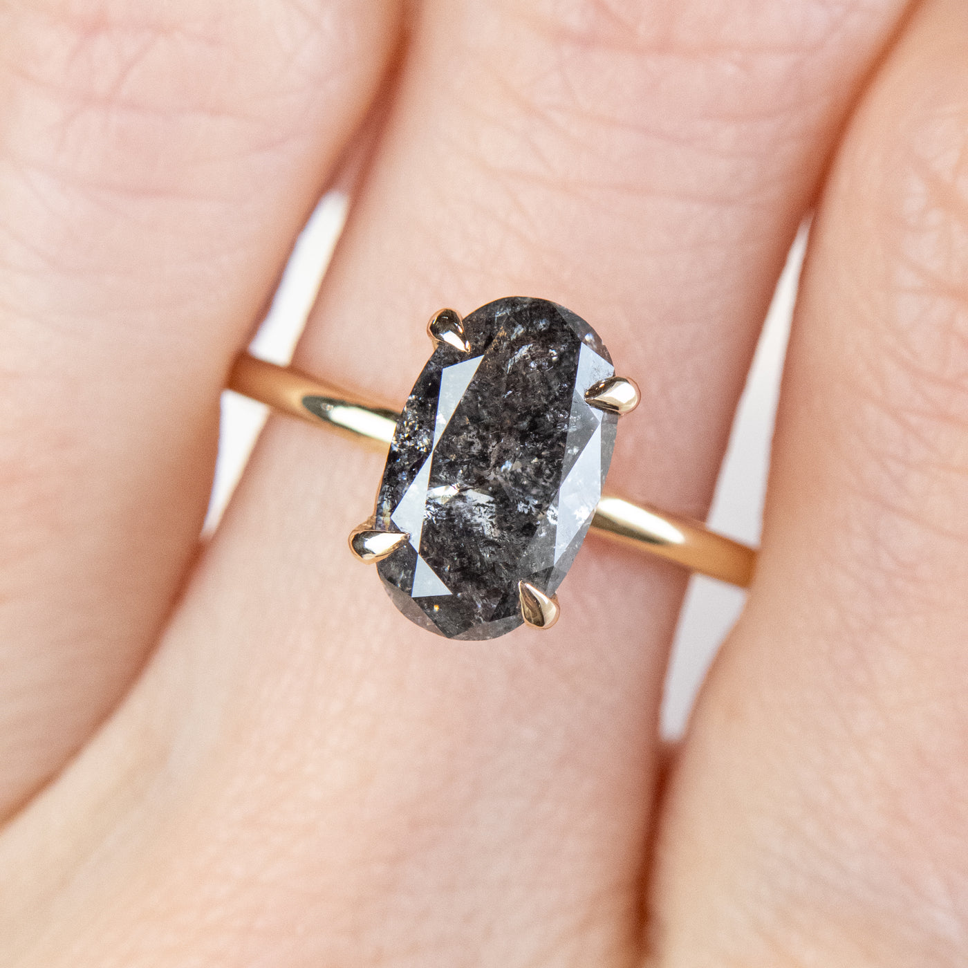 An elegant gold ring set with a large oval salt and pepper diamond. It features tiger-style prongs atop a decorative under basket, worn on a hand. 