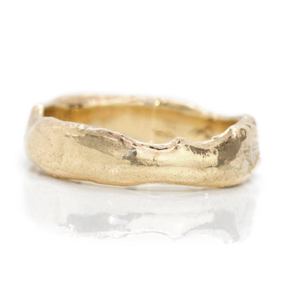 Close-up of a textured gold ring with an organic, uneven edge, reflecting light on a smooth surface.