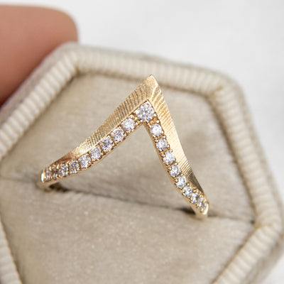 Elegant gold ring with a V-shaped design, encrusted with sparkling diamonds along the band shown resting in a white velvet ring box.