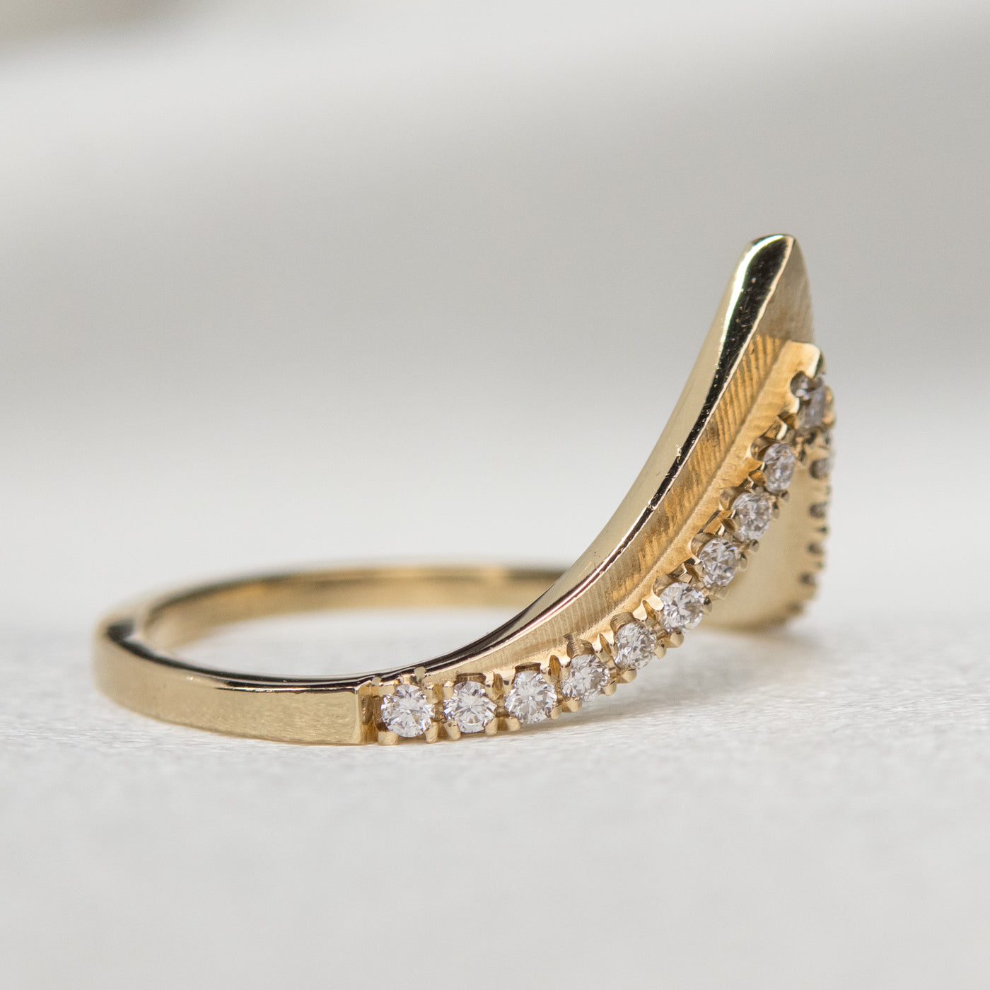 Elegant gold ring with a V-shaped design, encrusted with sparkling diamonds along the band, shown from the side.