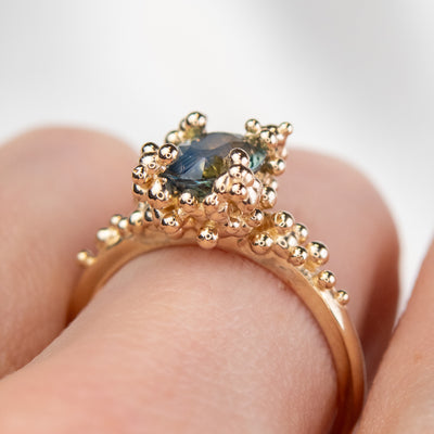 Side view of a gold ring with a cluster of small round gold beads holds an oval green sapphire at the center