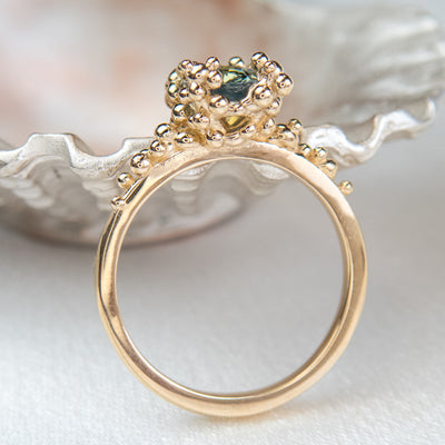 Side view of a gold ring with a cluster of small round gold beads holds an oval green sapphire at the center.