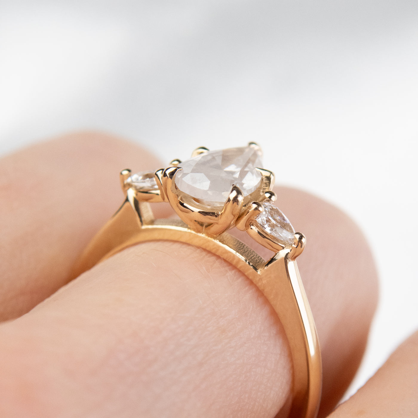 A three stone ring with a central pear-shaped diamond set in gold , flanked by two smaller pear diamonds, worn on a hand. 
