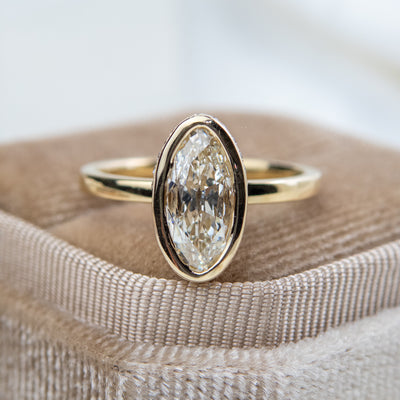 An elongated antique marquise-cut diamond ring bezel set with a polished gold band sits elegantly on a soft, velvet ring box. 