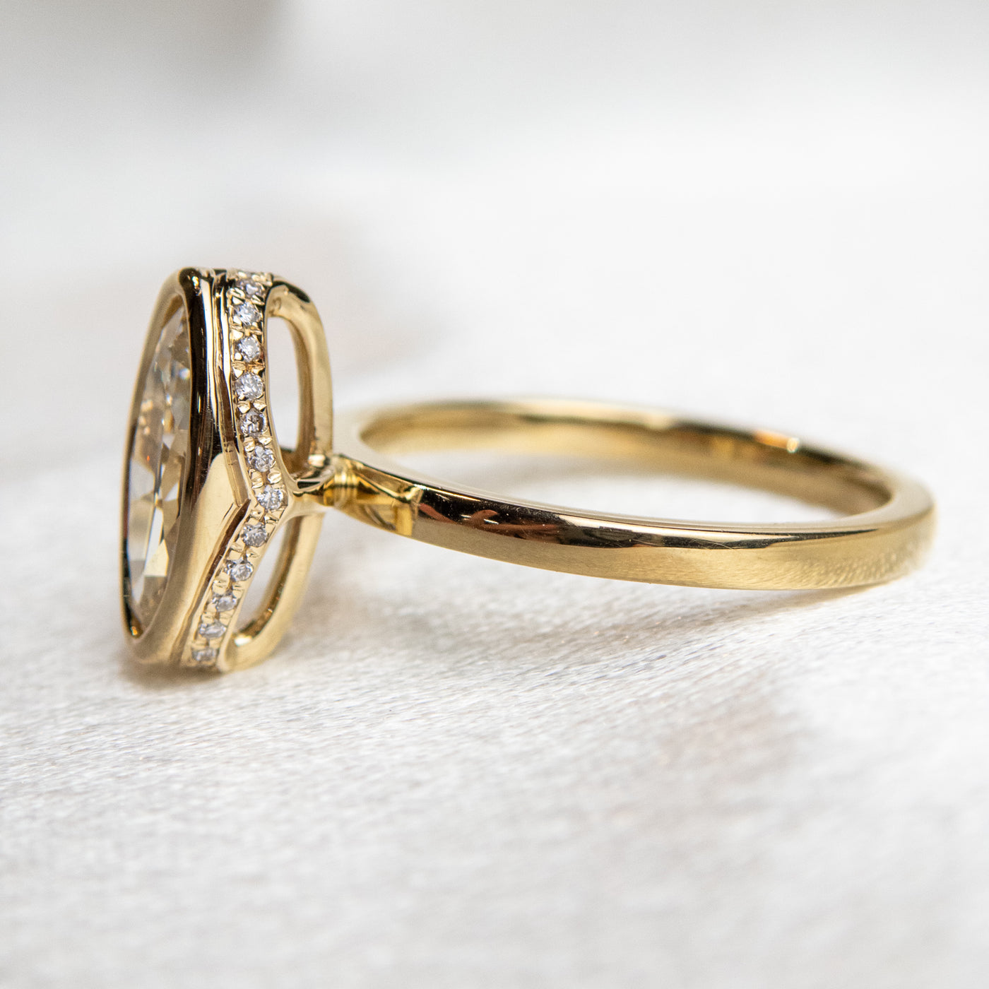 A side view of an elongated marquise-cut diamond ring bezel set with a polished gold band sits elegantly on a soft, white surface.
