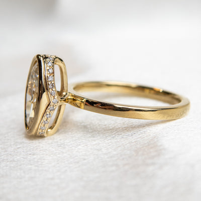 A side view of an elongated marquise-cut diamond ring bezel set with a polished gold band sits elegantly on a soft, white surface.